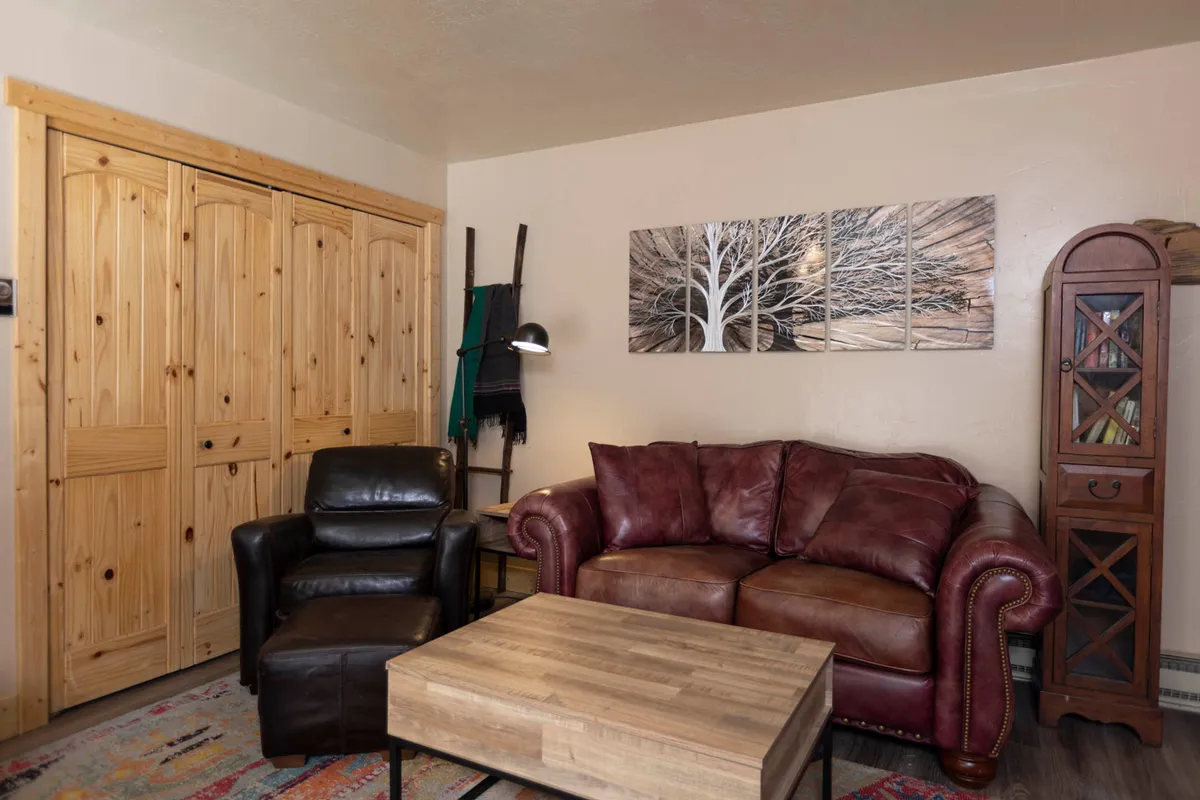 A comfortable, tastefully decorated living room featuring a brown leather sofa, wooden coffee table, black leather chair, prominent wall art, and a wooden cabinet. The arrangement lends itself to intimate gatherings or quiet evenings, enhanced by soft lighting and thoughtful decor.