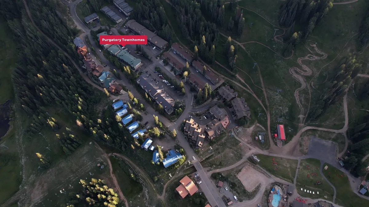 A welcoming exterior perspective of Purgatory Townhomes surrounded by forest, with ski trails visible nearby and a parking area for easy arrival. The setting emphasizes the blend of accessibility and immersion in nature, ideal for families or groups gathering for mountain adventures.