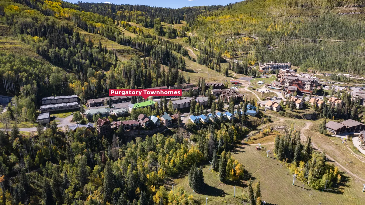 A wide exterior shot of Purgatory Townhomes set against a dramatic mountain landscape. The scene is framed by colorful autumn foliage and lush greenery, with the townhomes nestled harmoniously within the natural environment.