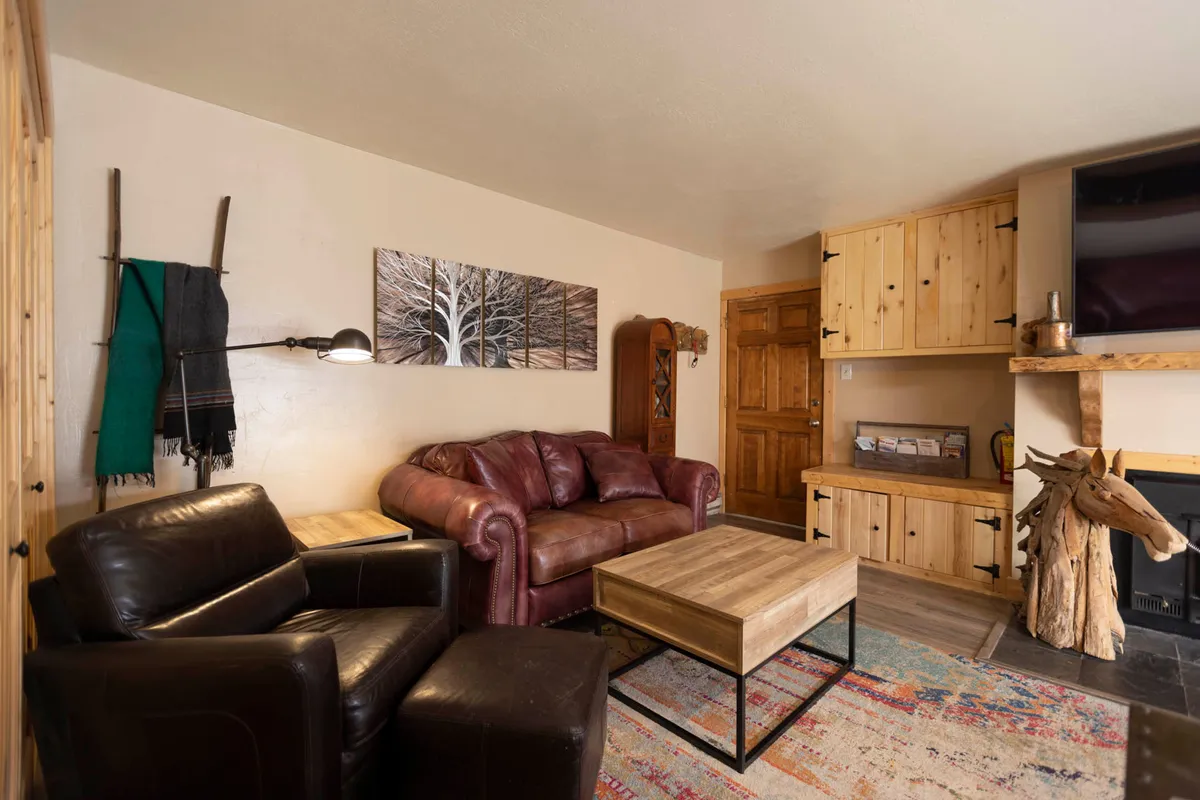 A stylish living area with a leather sofa, wooden coffee table, decorative artwork, and wooden cabinets. The ambiance is enhanced by the suggestion of a fireplace or cozy gathering spot ideal for game nights or sipping cocoa after a day outdoors.