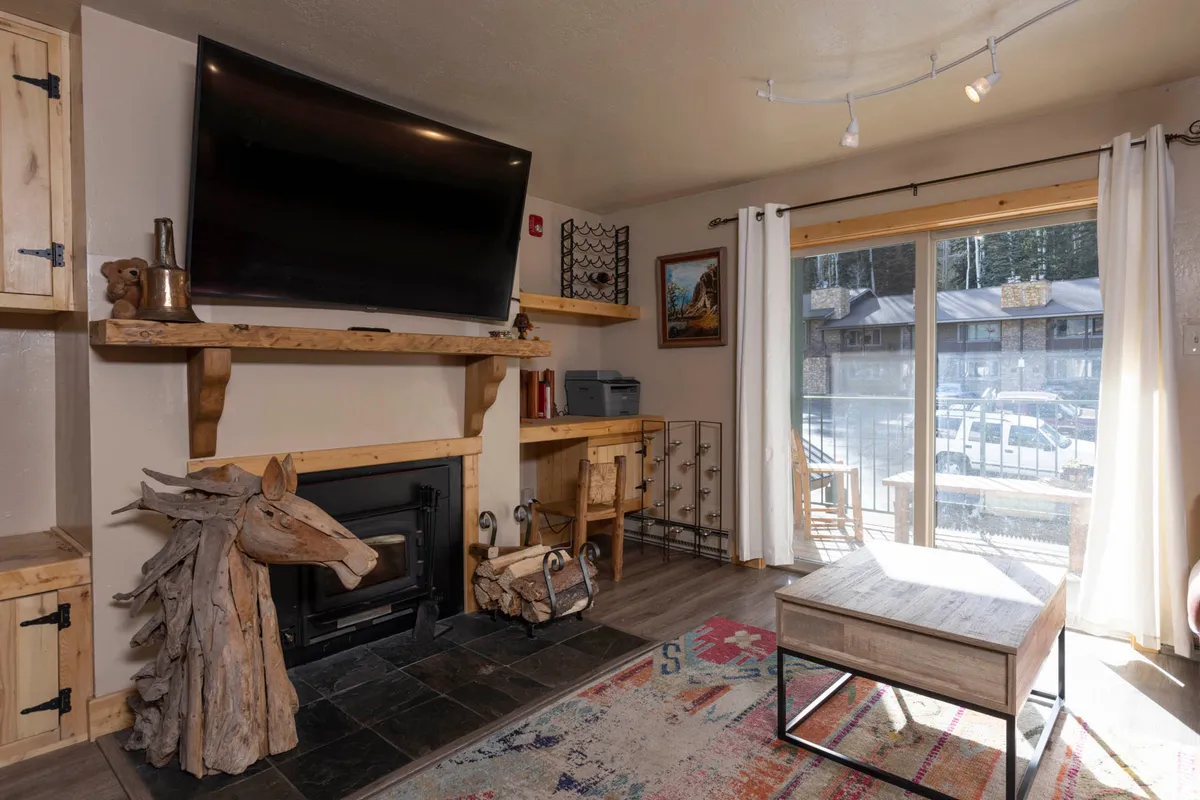A warm, welcoming living space featuring a fireplace, large TV, wooden horse sculpture, and a sliding glass door, offering a sense of comfort and a connection to the outdoors. The arrangement promotes relaxation, group gatherings, and cozy evenings after skiing.